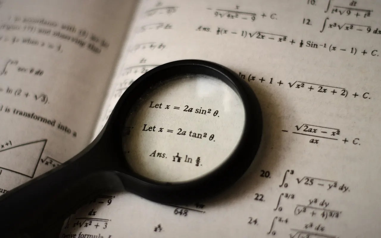 Magnifying glass over the pages of a book full of formulas, in black and white