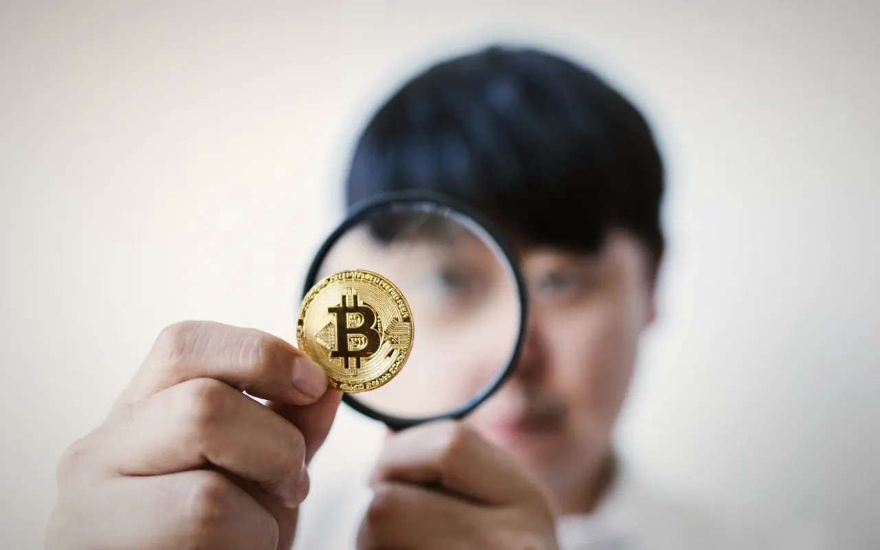 Man looking at a bitcoin coin through a magnifying glass
