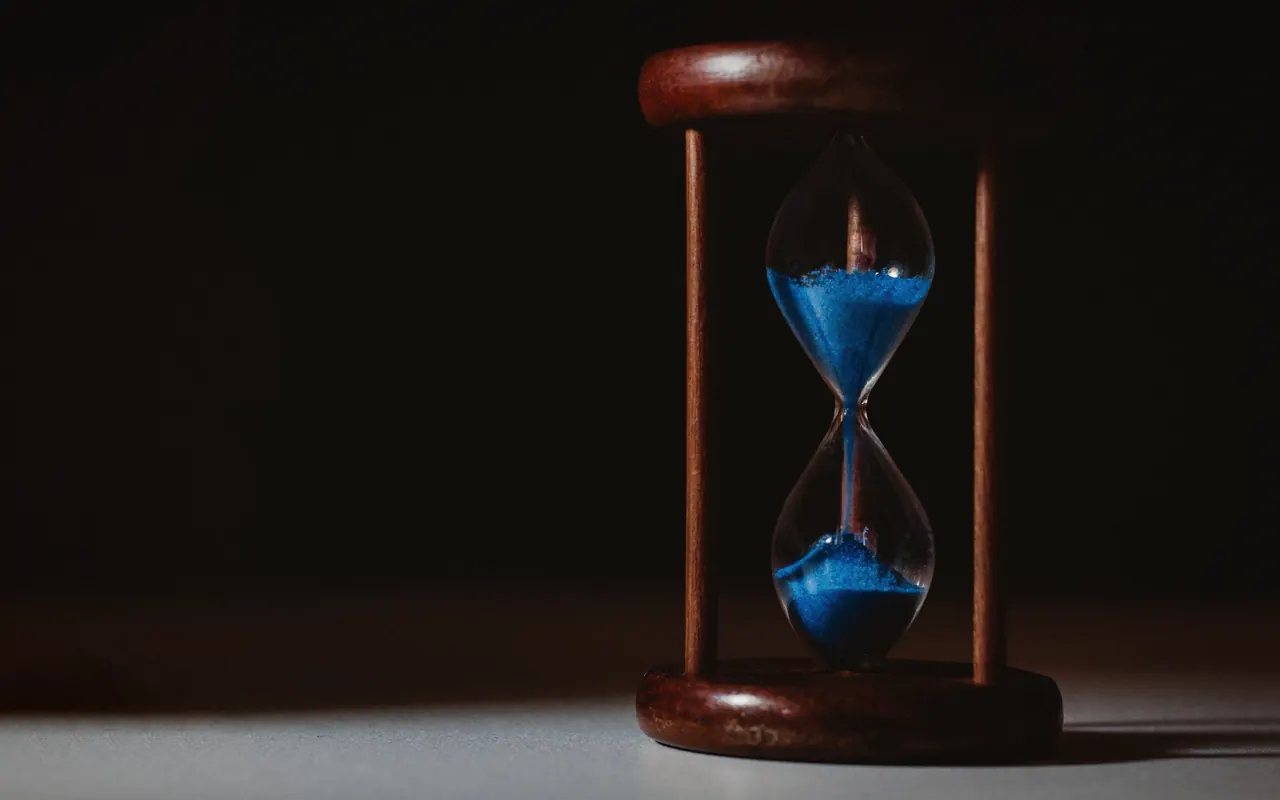 Hourglass with blue sand on a dark wooden table